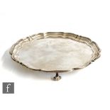 A hallmarked silver circular salver with scalloped borders and raised on four scroll feet,