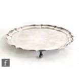 A hallmarked silver circular salver of plain form with scallop border and raised on three scroll