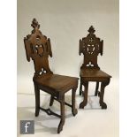 A pair of Victorian carved oak hall chairs in the ecclesiastical style, the plank seats on shaped