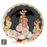 Carlton Ware - An Art Deco charger decorated in the Hollyhocks pattern against a black ground,