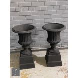 A small pair of cast iron black painted campana shaped terrace urns each on a square base, height