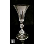 An 18th Century drinking glass circa 1730, the flared bell form bowl above medial knop, falling to a