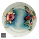 A Moorcroft side plate decorated in the Frilled Orchid pattern against a green wash ground,