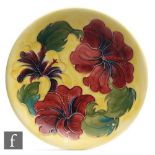 A Moorcroft Pottery plate decorated in the Hibiscus pattern against a yellow ground, impressed