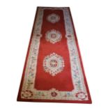 A set of three red/pink ground woollen Runners, each with a cream ground floral border and three