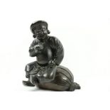 A heavy Chinese bronze Group, modelled as a jolly faced man seated on a large sack and holding a