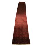 An Oriental red ground woollen Runner, with all over diamond design inside a conforming border,