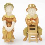 Pair of Royal Worcester blush ivory and gilded porcelain figures modelled as a seated boy and