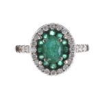 18k white gold emerald and diamond oval cluster ring, the centre emerald 0.50ct approx, within a
