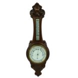 Oak aneroid barometer/thermometer, the 8" white dial within a foliate carved case
