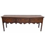 George III oak low dresser, the planked moulded top over three long drawers and a wavy frieze,