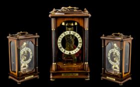 A Modern Skeleton Clock with Franz Hermle with a mahogany finish glass case with brass carrying