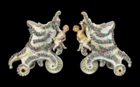 Pair of German Vases cornucopia shape on rolling wheels, with cherubs to front.