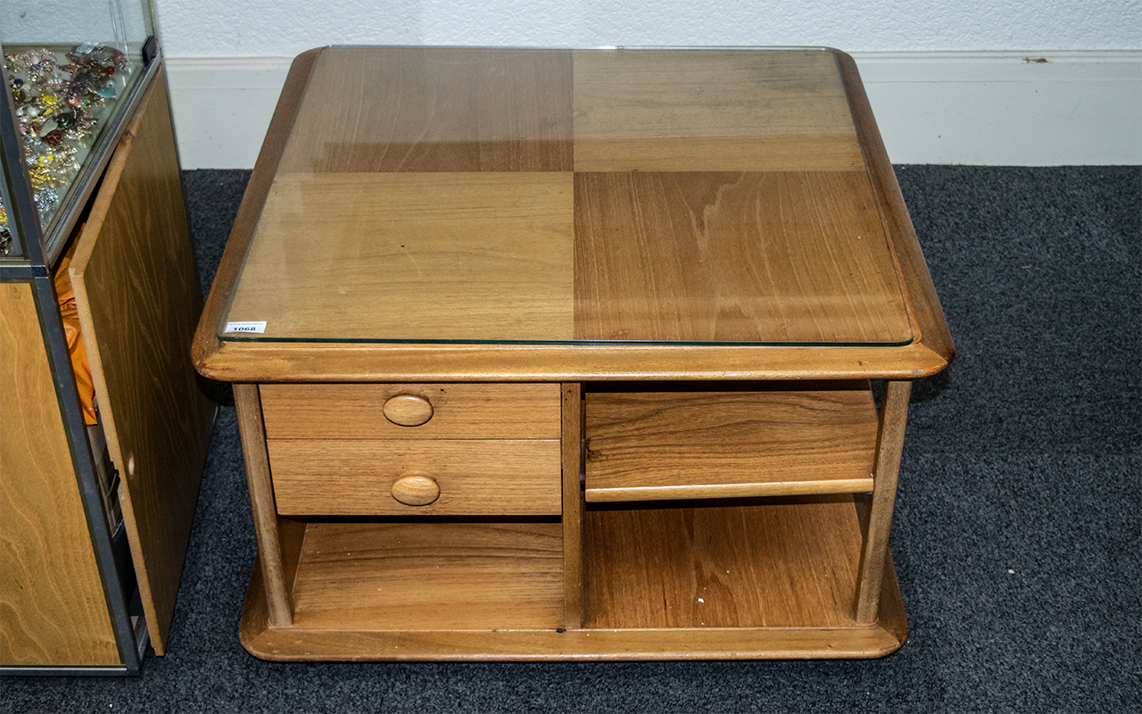 An Ercol Coffee Table, square form, with shelves and drawers, raised on casters, with glass top.