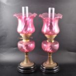 A pair of cranberry glass oil lamps with fluted shades and reservoirs.