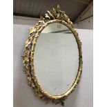 An oval wall mirror, in a gilt gesso vine leaf surround