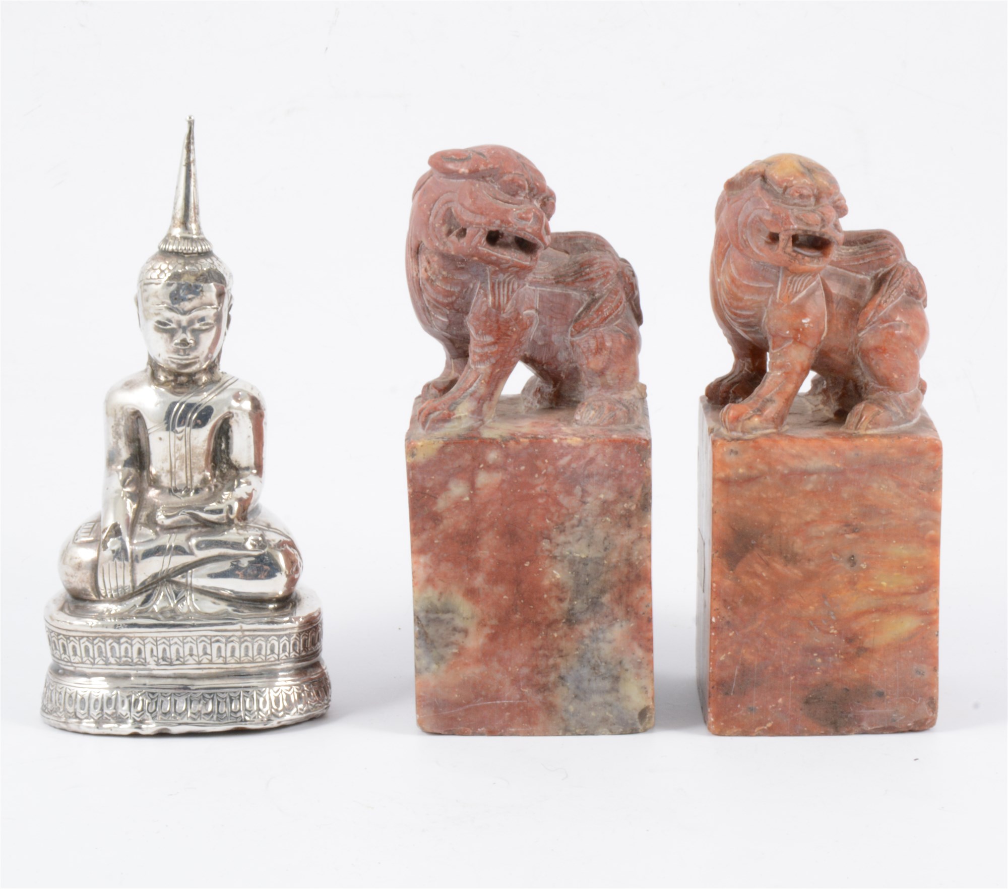 Two carved red stone scroll weights and a white metal Eastern figure of Buddha