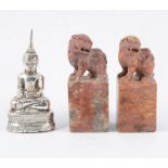 Two carved red stone scroll weights and a white metal Eastern figure of Buddha