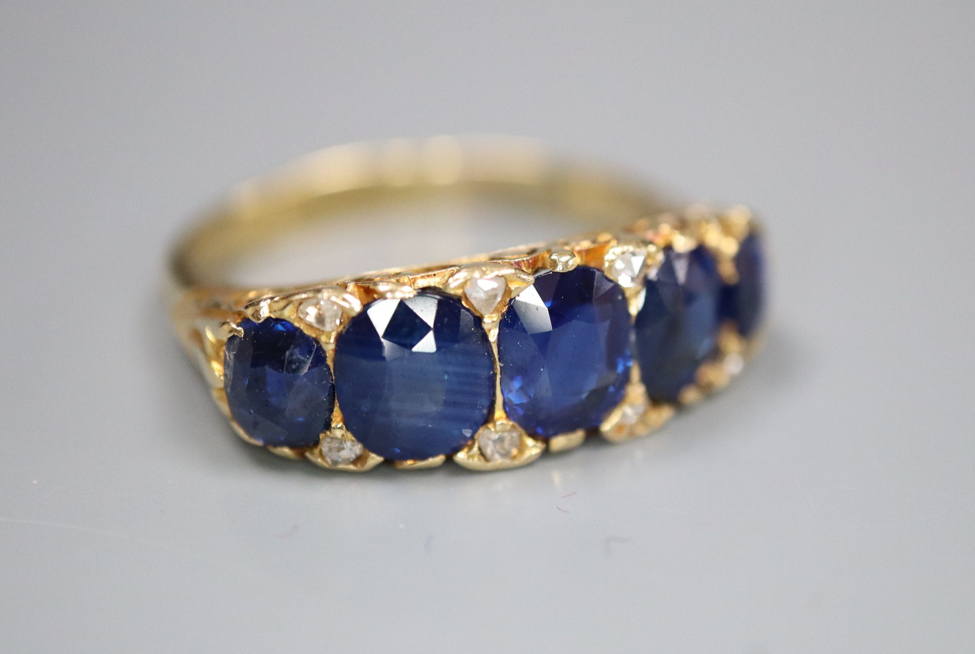 A George V 18ct gold and graduated five stone sapphire set half hoop ring, with diamond chip