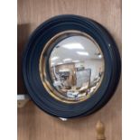 An ebonised framed convex mirror, with a gilt slip