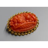 An antique yellow metal mounted oval coral set brooch, carved with a basket of flowers and fruit,