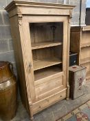 A pine display cabinet, fitted single glazed door enclosing four shelves over base drawer, width