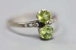 An 18ct and plat, two stone peridot crossover ring, with diamond set shoulders, size W, gross 2.7