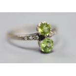 An 18ct and plat, two stone peridot crossover ring, with diamond set shoulders, size W, gross 2.7