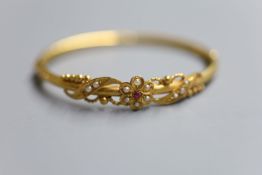 A late Victorian yellow metal, ruby and seed pearl set hinged bangle, gross 10.6 grams.CONDITION: