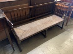 An Arts and Crafts oak framed rush seated settee, with turned supports and spindle back, length