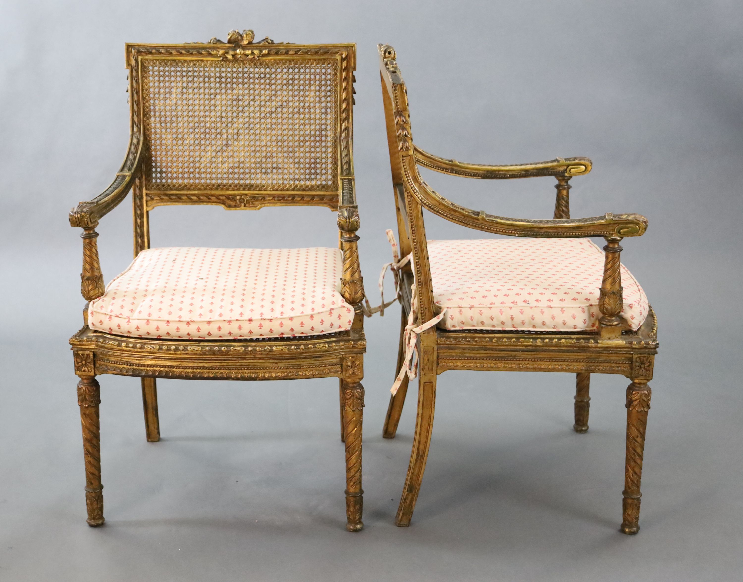 A pair of Louis XVI style walnut giltwood fauteuils, with flower and ribbon carved frames, caned