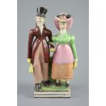 A Staffordshire pearlware group of a Dandy and Dandizette, c.1820, standing before rockwork on a