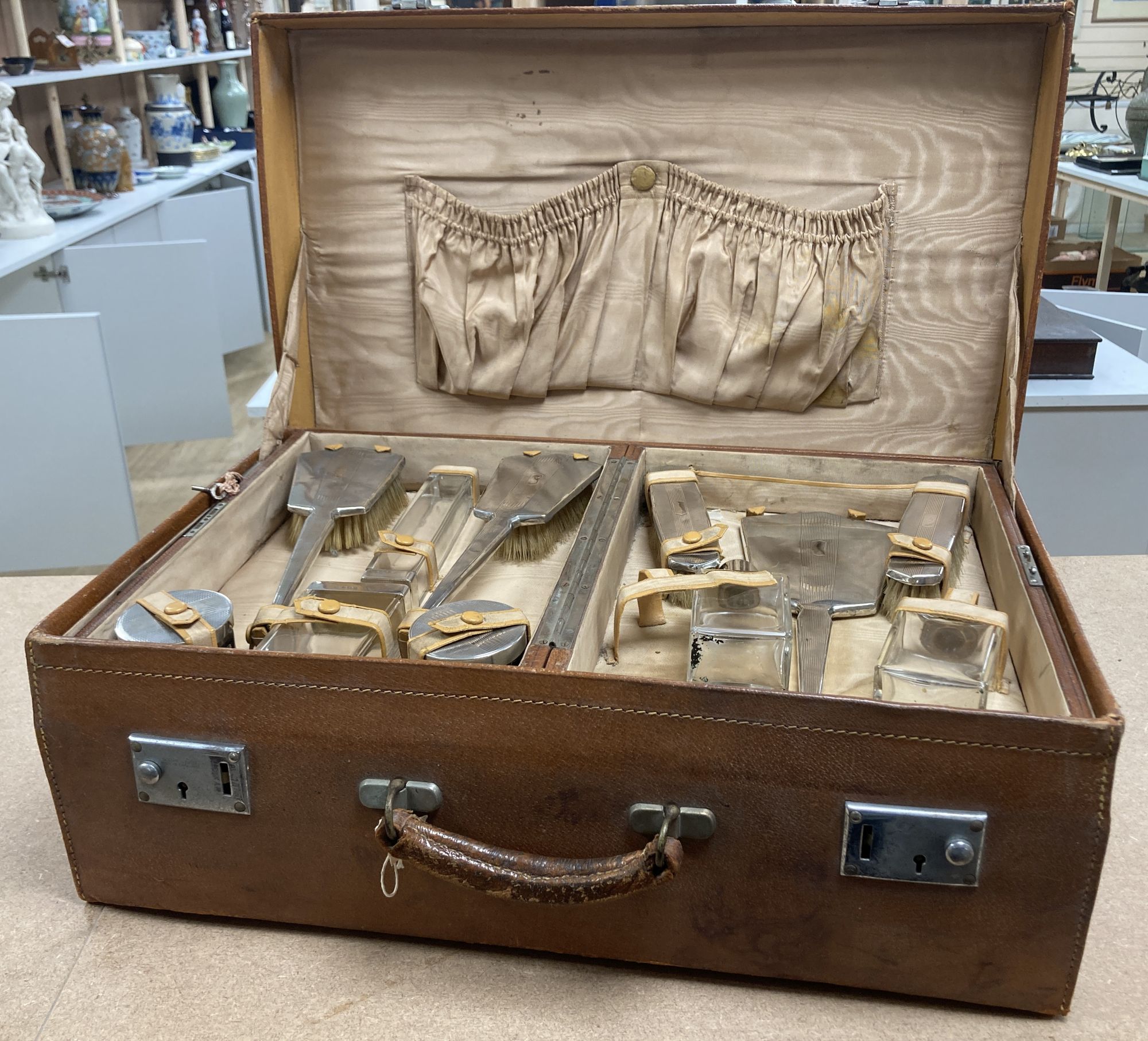 A 1930's Art Deco leather travelling toilet case, containing eleven silver mounted jars, mirror, and