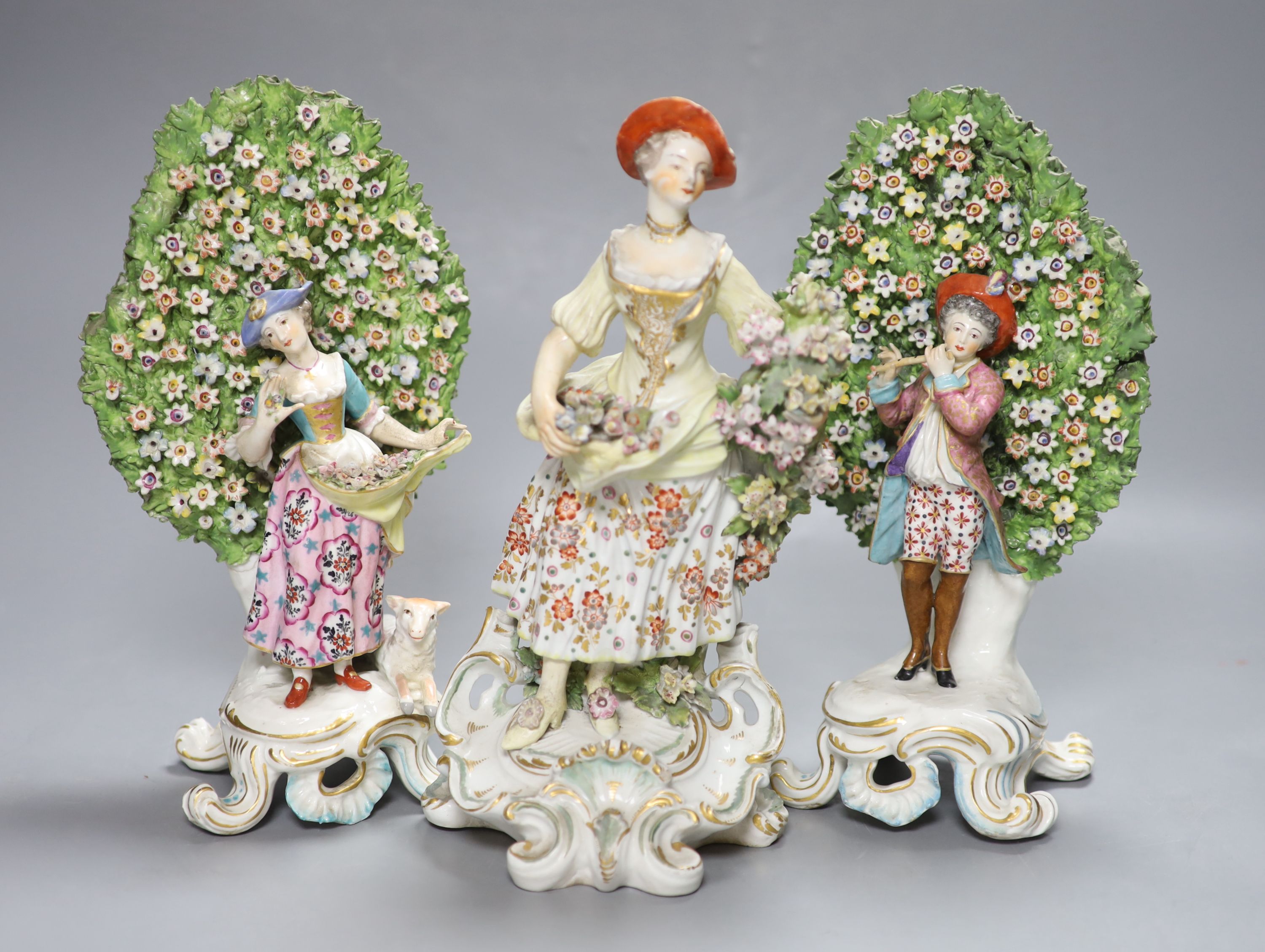 An 18th century Derby figure of a flower seller and a pair of French porcelain bocage groups,