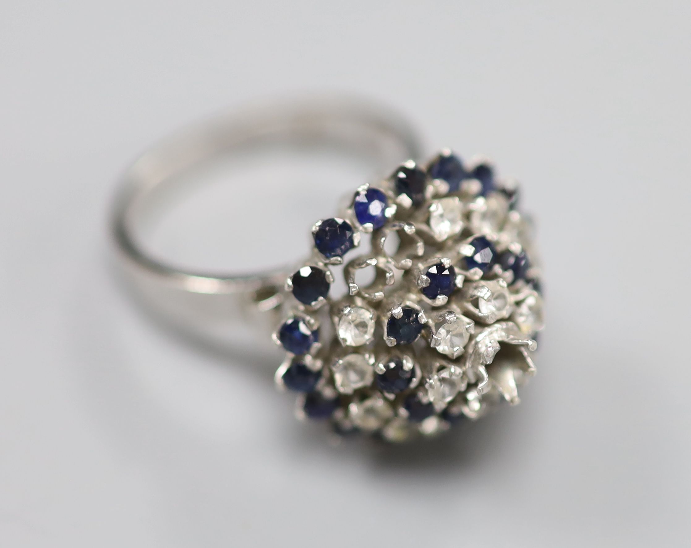 A white metal (stamped 18k) and two colour sapphire? set raised cluster ring, size K/L, gross 5.2