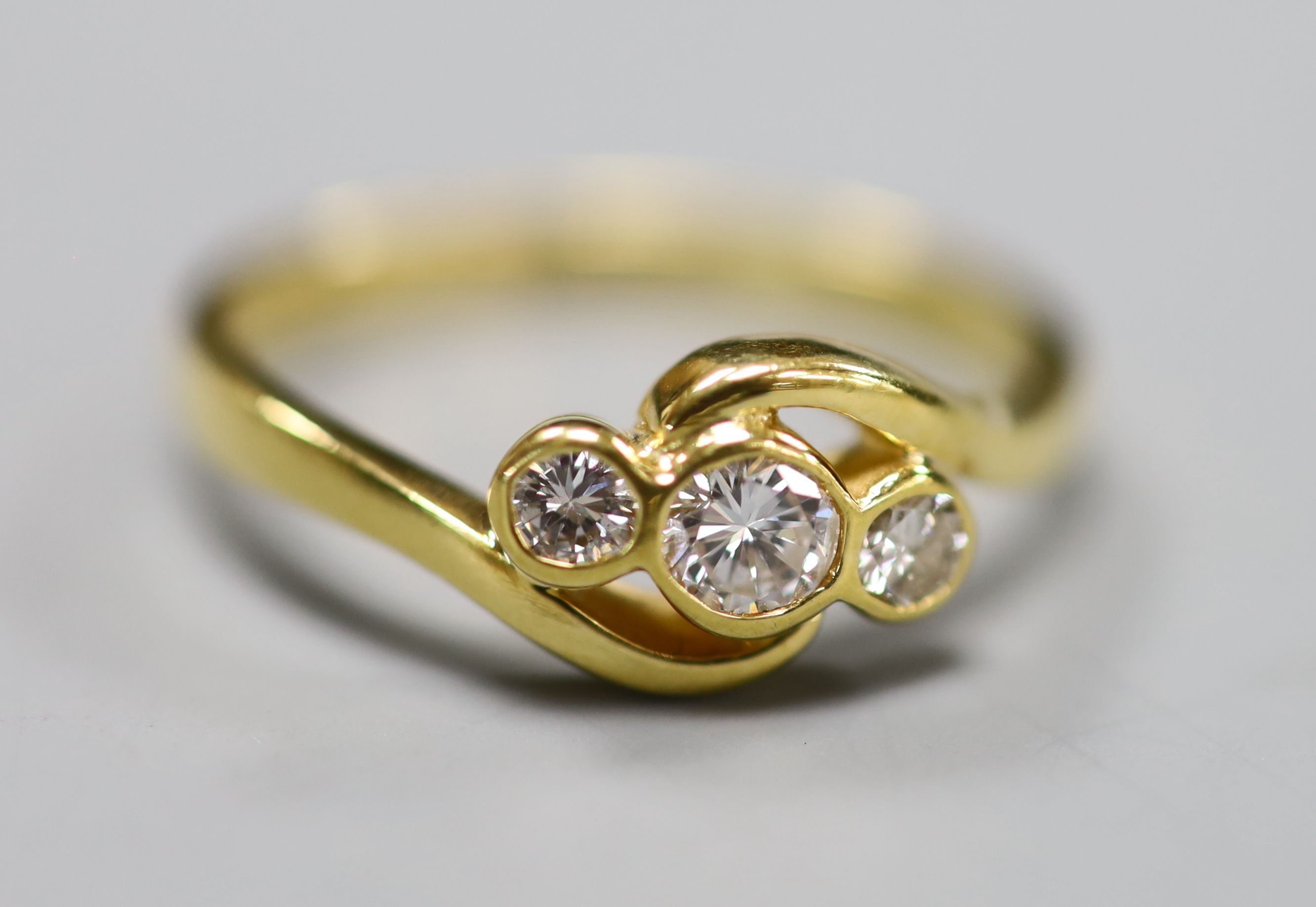 A modern 18ct gold and three stone diamond set crossover ring, size N, gross 3 grams.