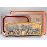 An African hardwood carving of a herd of elephants, and two papier mache trays, largest 46cm