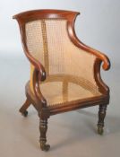 A Regency mahogany bergere armchair, with scroll carved frame, on turned legs fitted brass