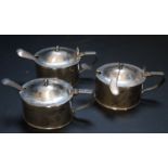 A set of three Edwardian silver mustard pots, plain oval, the hinged covers with shell
