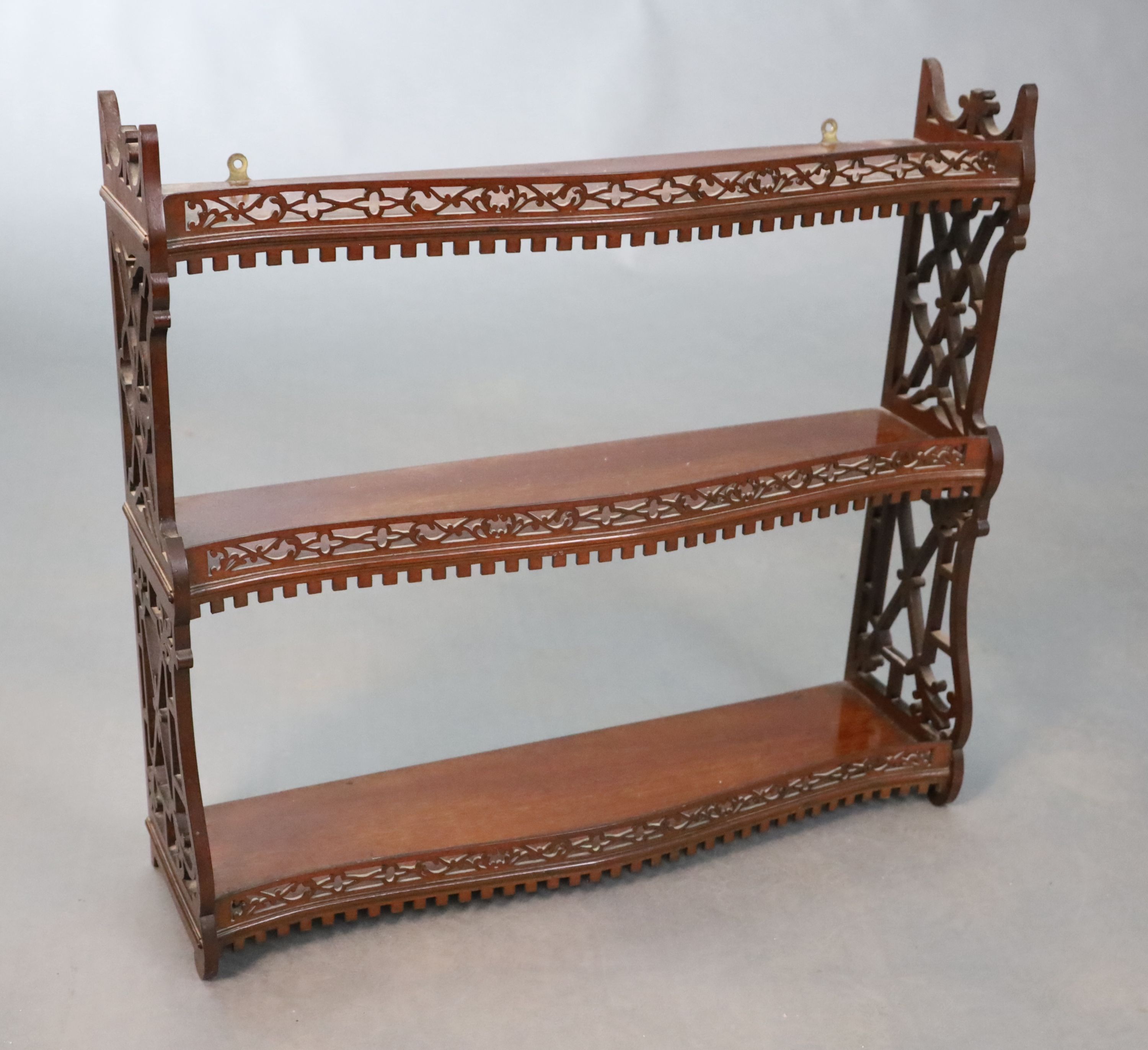 A George II style mahogany three tier wall shelf, with a dentil moulded apron within fretted side