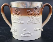 A Victorian silver mounted stoneware loving cup, decorated in relief with hunting motifs and topers,