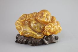 A Chinese amber figure of Buddha, 19th century, reclining in flowing robes, on a fitted carved
