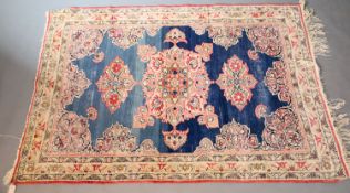 A Kerman Lavar rug, the blue field woven with pink stylised floral medallions, within a shaped