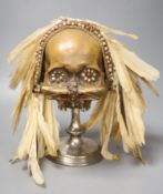 An Asmat ancestral skull, with beaded eyes and feather head-dress on stand