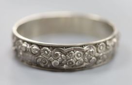 A continental white metal hinged bangle, decorated with continuous band of flowers and scrolls, 19