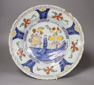 A large polychrome Delft charger, painted with a central figure beside a walled garden, set within