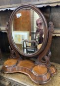 A Victorian mahogany toilet mirror of oval form above a raised platform with twin lidded