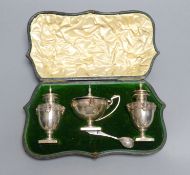 A cased Edwardian silver three piece condiment set and matching spoon, with Greek Key and mask