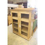 A modern glazed pine bookcase fitted two doors and shelves, length 114cm, depth 34cm, height 140cm
