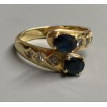 A modern 18ct and two stone sapphire crossover ring, with diamond set shoulders, size P, gross 5.4